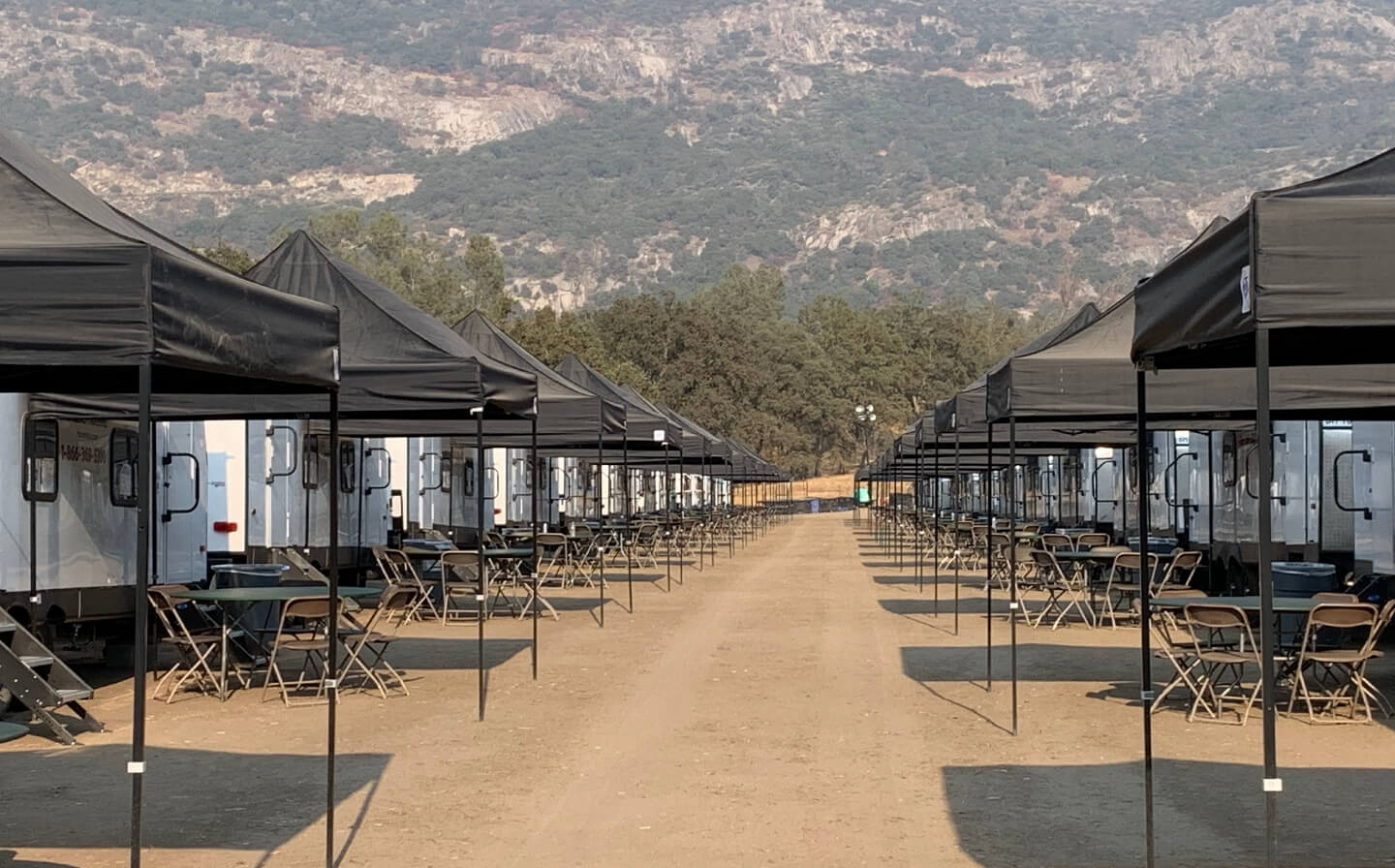 Trailers, tents, and tables arranged in a dirt area, showcasing the setup for base camp construction.