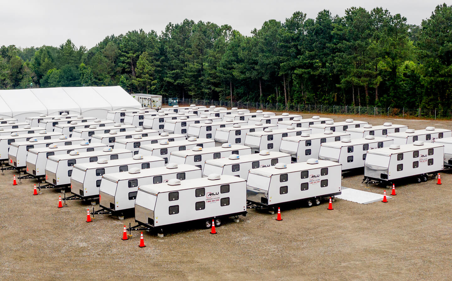 A large group of white trailers parked in a grassy field to form a base camp.
