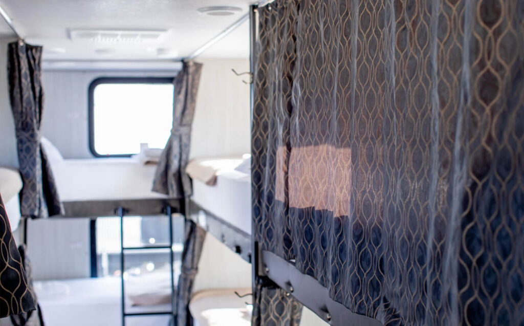 Inside a temporary housing trailer, a small room features a bunk bed with curtains for a base camp.