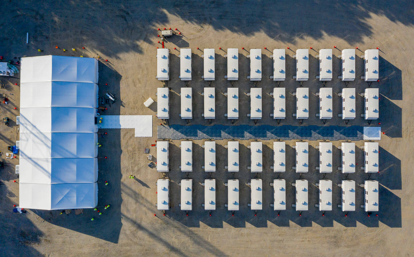 Aerial perspective of a large tent with numerous white trailers, set up for disaster response base camp operations.