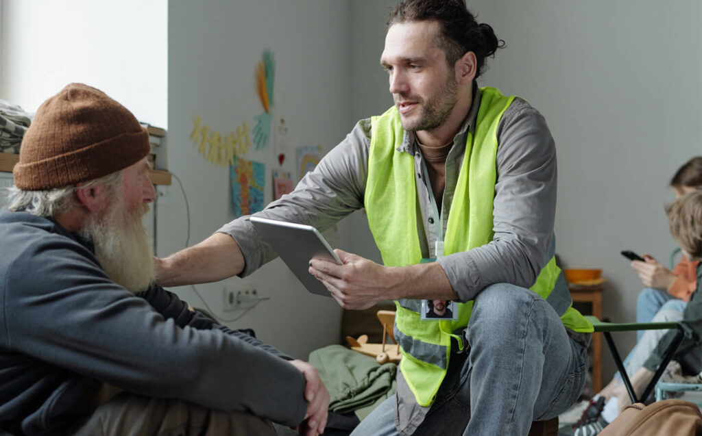 A post-disaster shelter staff member in a safety vest talks to a man, offering assistance and support.